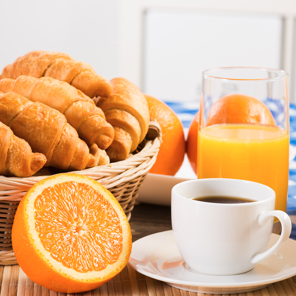 O que são commodities? : mesa de café da manhã com cesta de pães, suco de laranja e xícara de café.