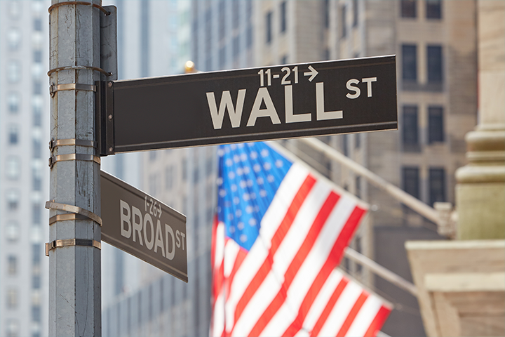 Diversificação de investimentos: imagem mostra placa da rua de Wallstreet com bandeira estadunidense ao fundo. 