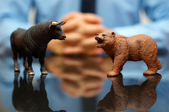 Bull market: Mesa de vidro com duas esculturas: um touro e um urso. Ao fundo, está um homem com as mãos cruzadas.
