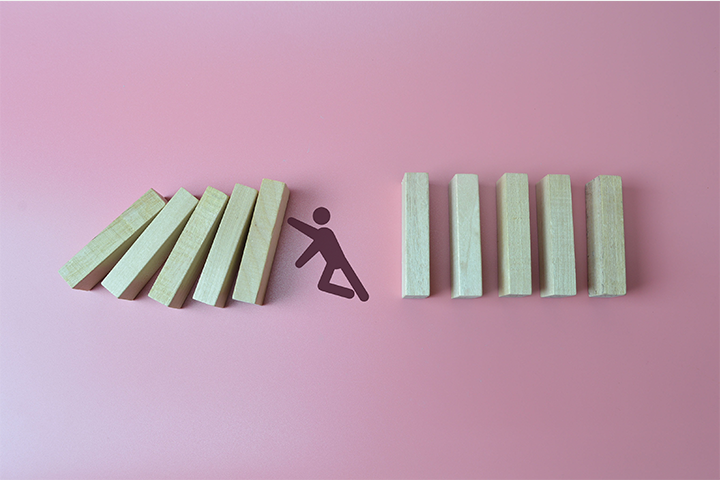 Estagflação: peças de madeira em formato retangular caindo. Há um desenho de um boneco tentando impedir que uma peça derrube a outra. 