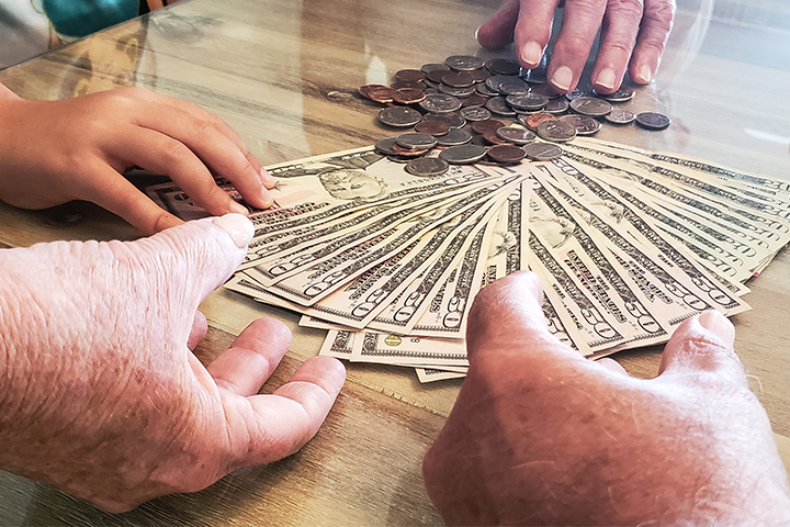 Subscrição de ações: imagem mostra notas de 50 dólares e moedas espalhadas sobre uma mesa de madeira. Mãos femininas e masculinas estão dividindo o dinheiro.
